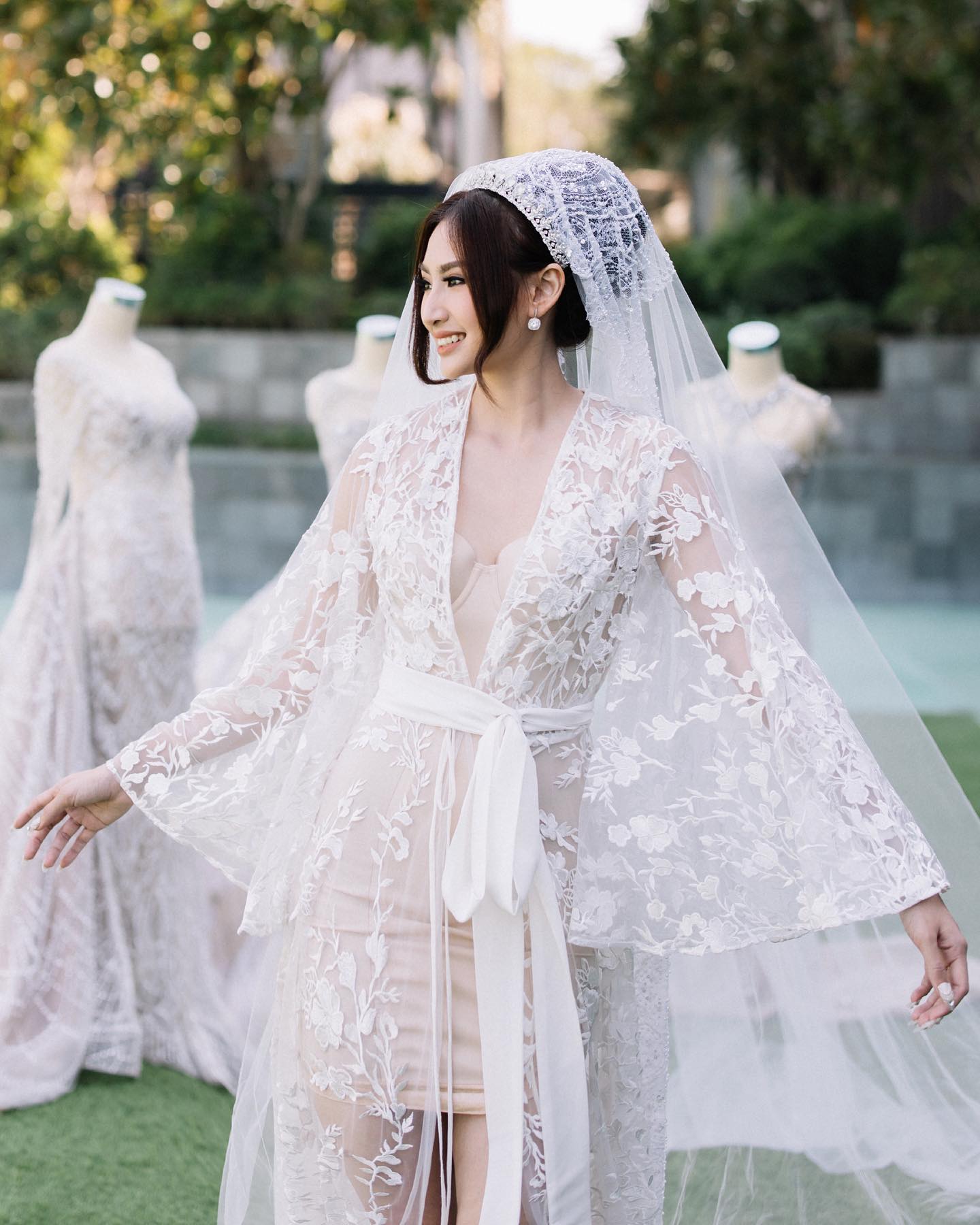Woman wearing a white lace wedding dress with a veil outdoors.