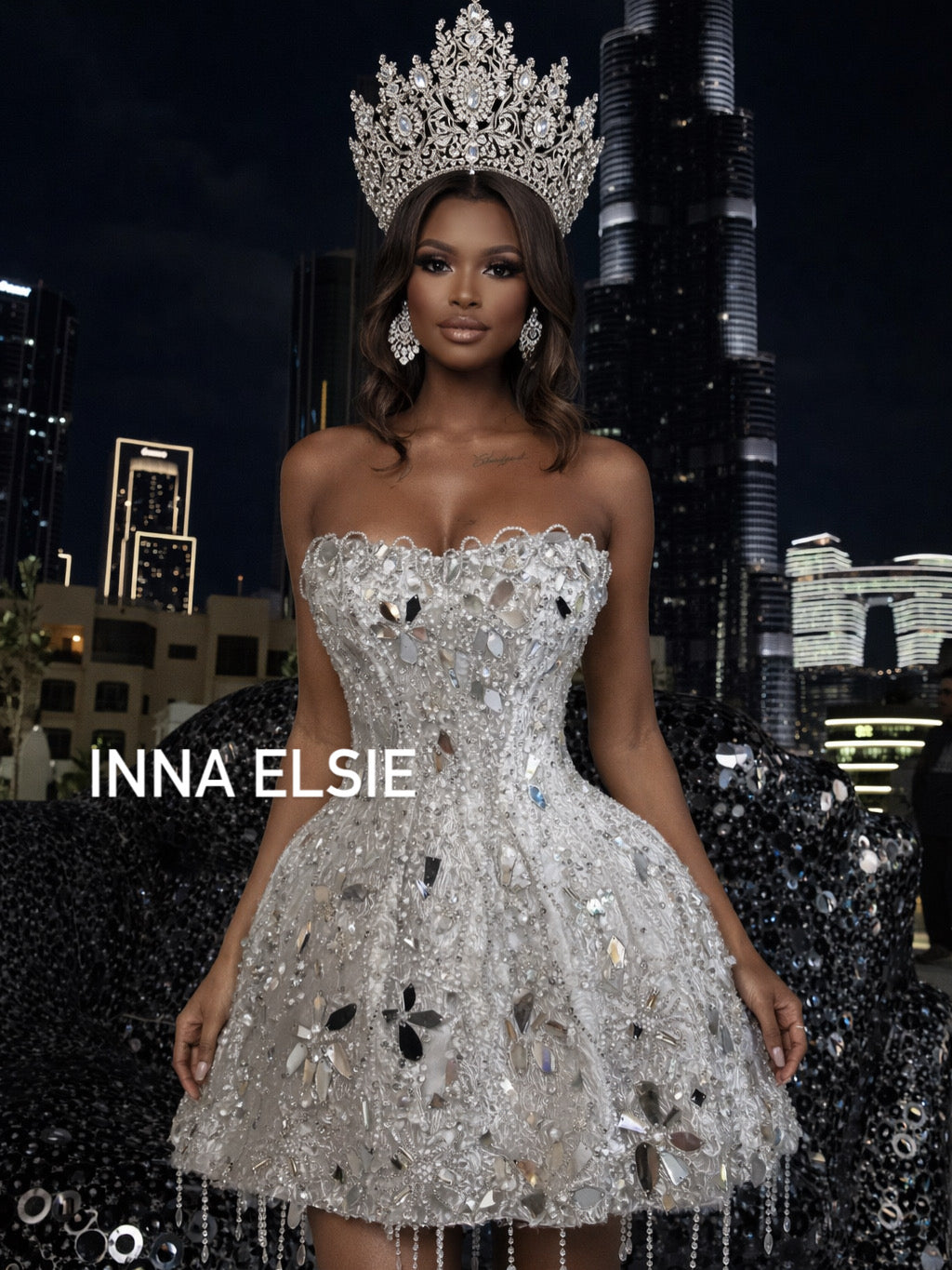 Woman in a sparkling silver dress and tiara against a cityscape background with 'INNA ELSIE' text.